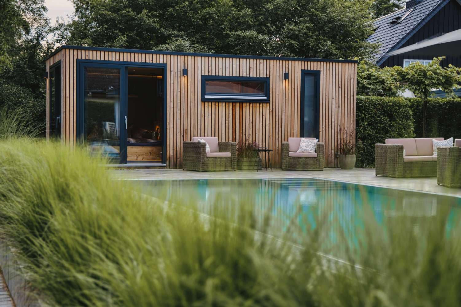 Moderne Gartensauna mit Holzfassade neben einer Terrasse und einem Pool